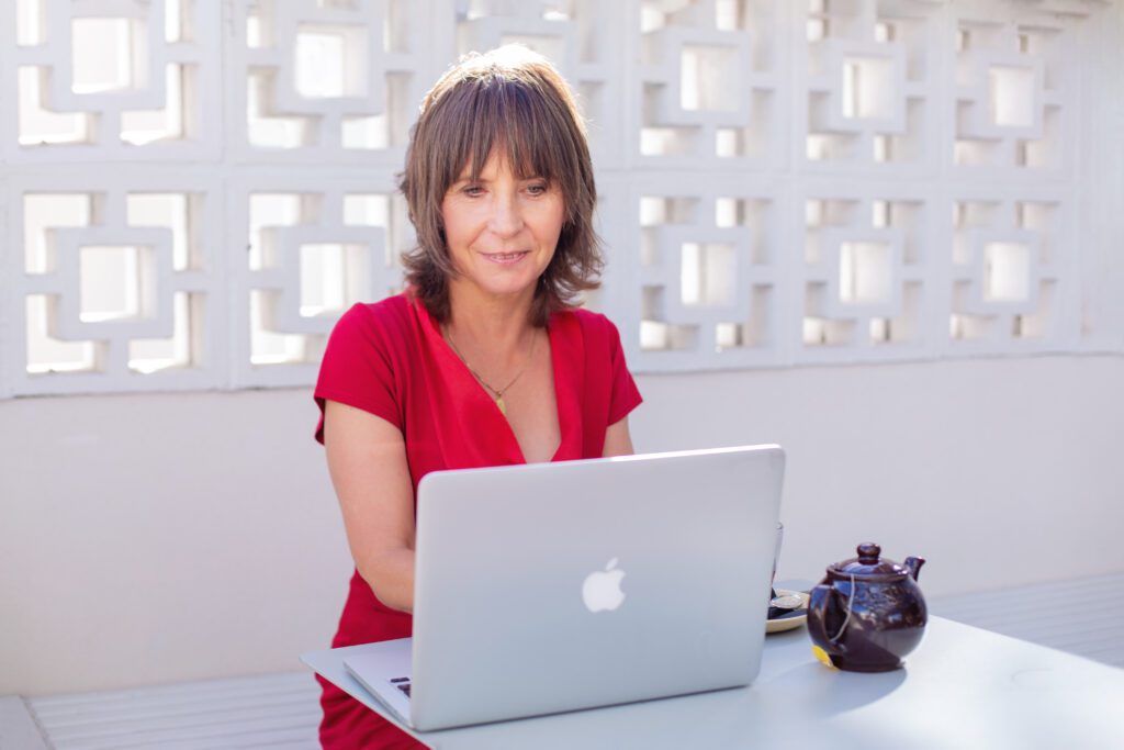 Suzan Joy Wells sitting outdoors with laptop and tea